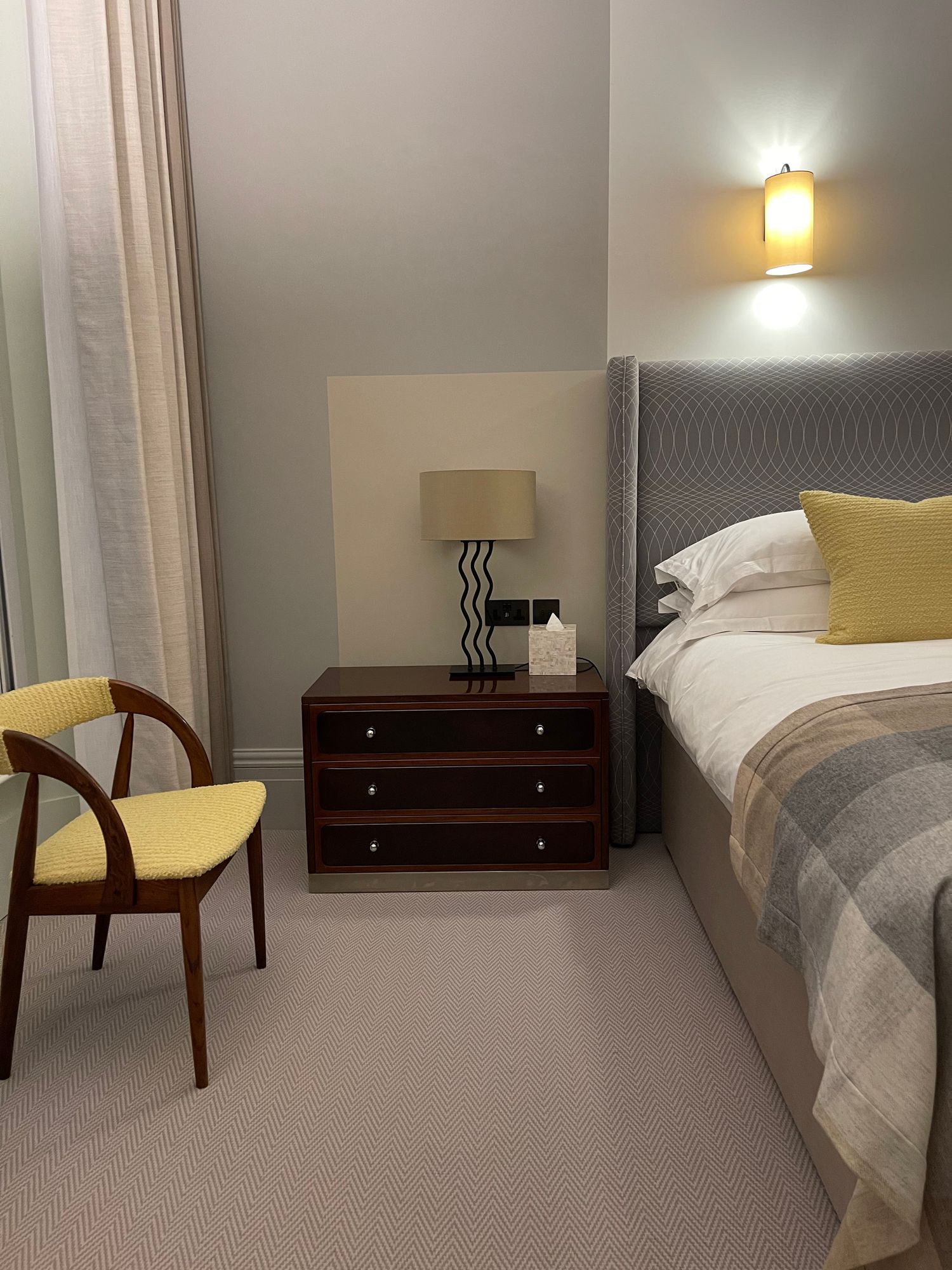 Two wooden chairs with yellow seats beside a dark wood bedside chest in a finished guest room at Brown's Hotel, Mayfair.
