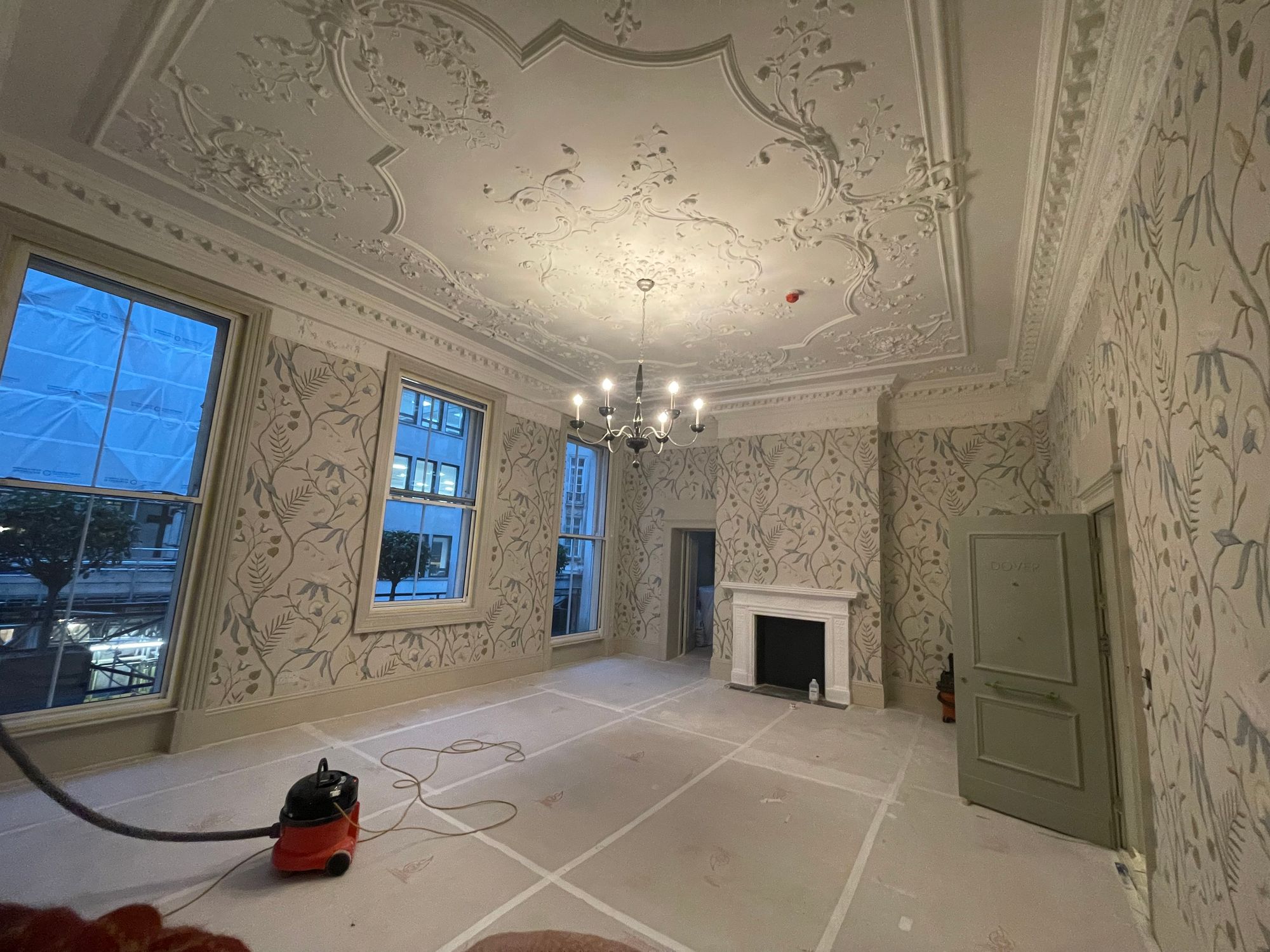 Room at Brown's Hotel, Mayfair, during works: Adam's Eden wallcovering hung beneath an ornate plaster ceiling and chandelier, with protection board on the floor and a vacuum cleaner in view.