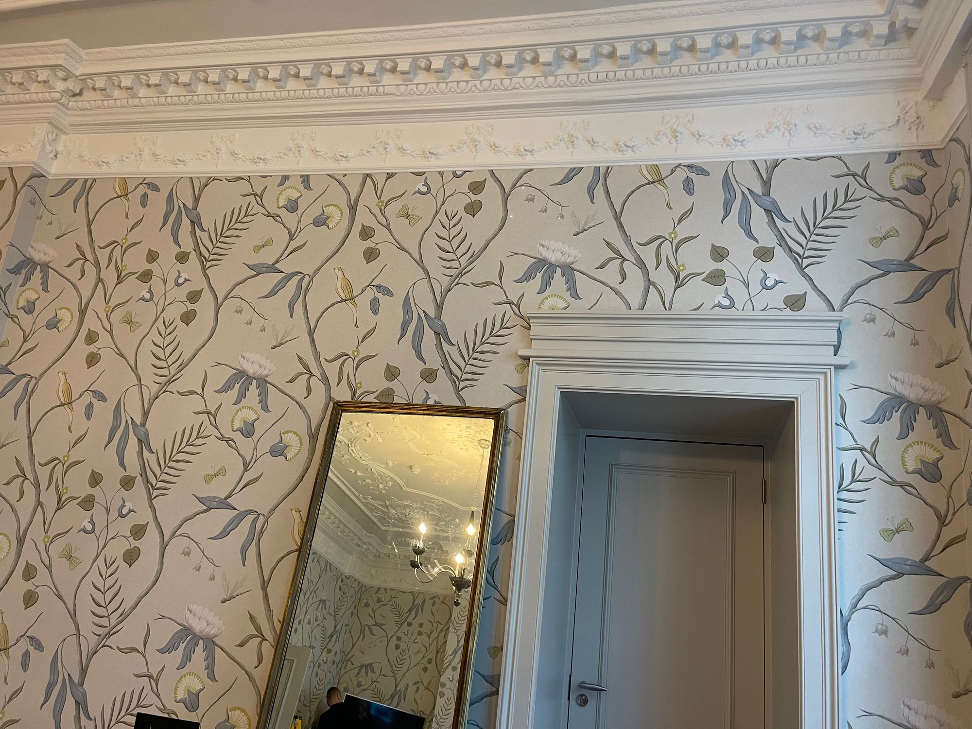 Adam's Eden wallcovering beneath a carved cornice at Brown's Hotel, Mayfair, around a door case, with a gilt mirror leaning against the wall.