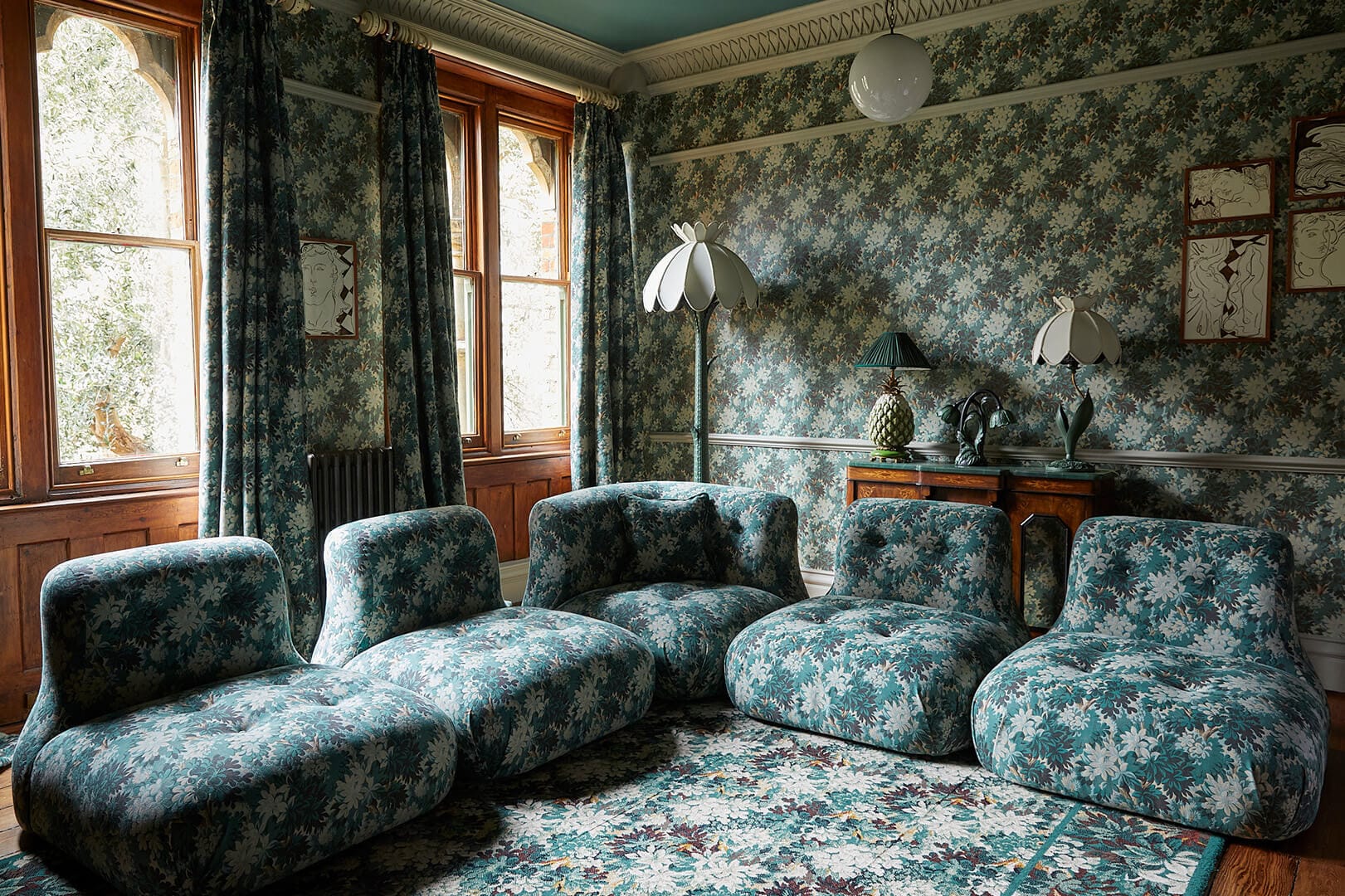 Finished room at the House of Hackney showroom, St Michael's Clergy House, with dark floral wallpaper, matching curtains and low floral sofas.