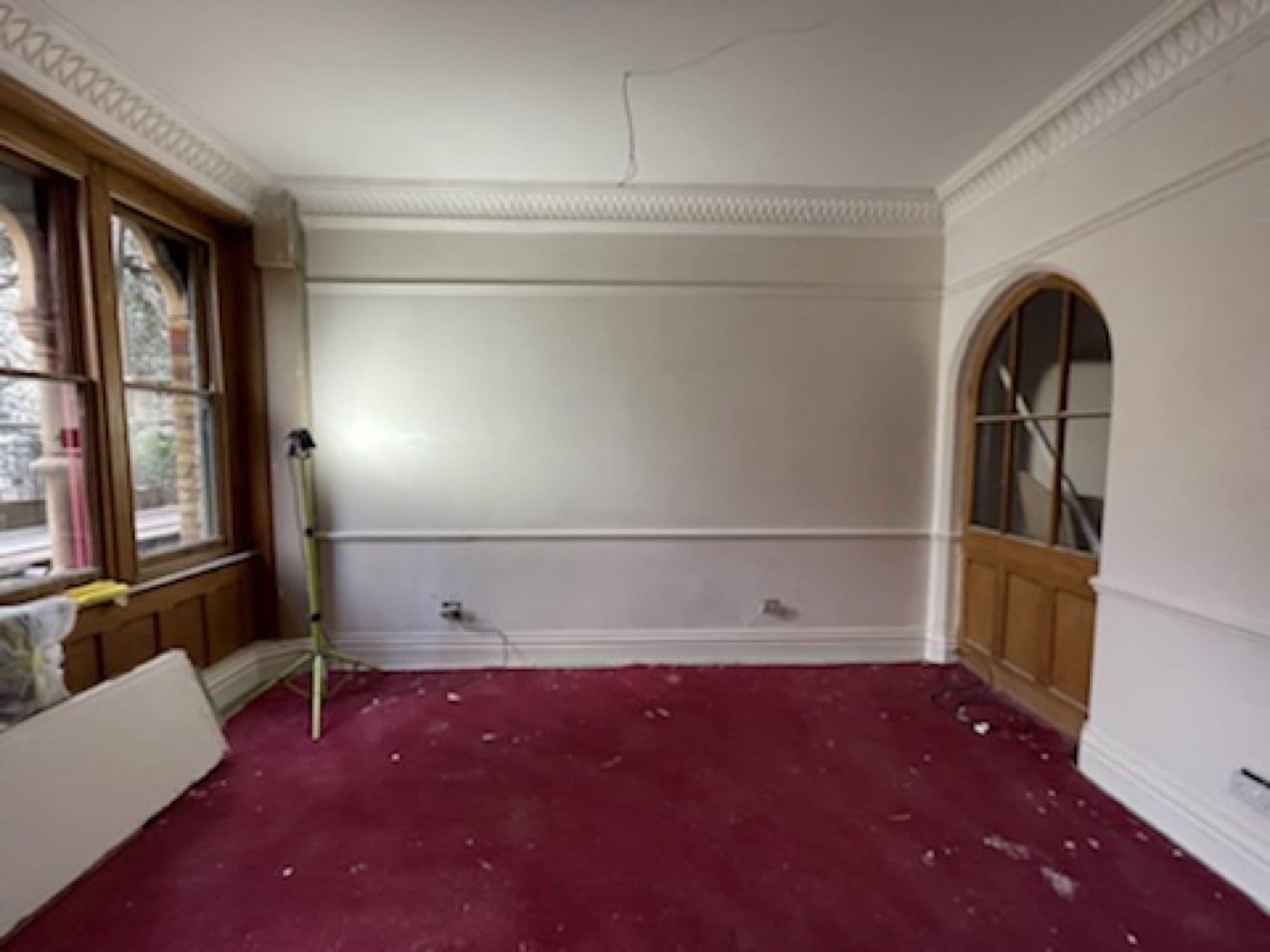 Before: an empty room at St Michael's Clergy House, with red carpet, white walls and an arched door, before the showroom works.