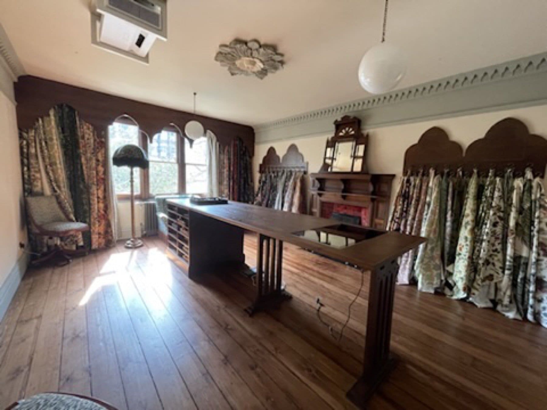 Finished room at the House of Hackney showroom, with a long timber table, hanging fabric samples and arched windows.