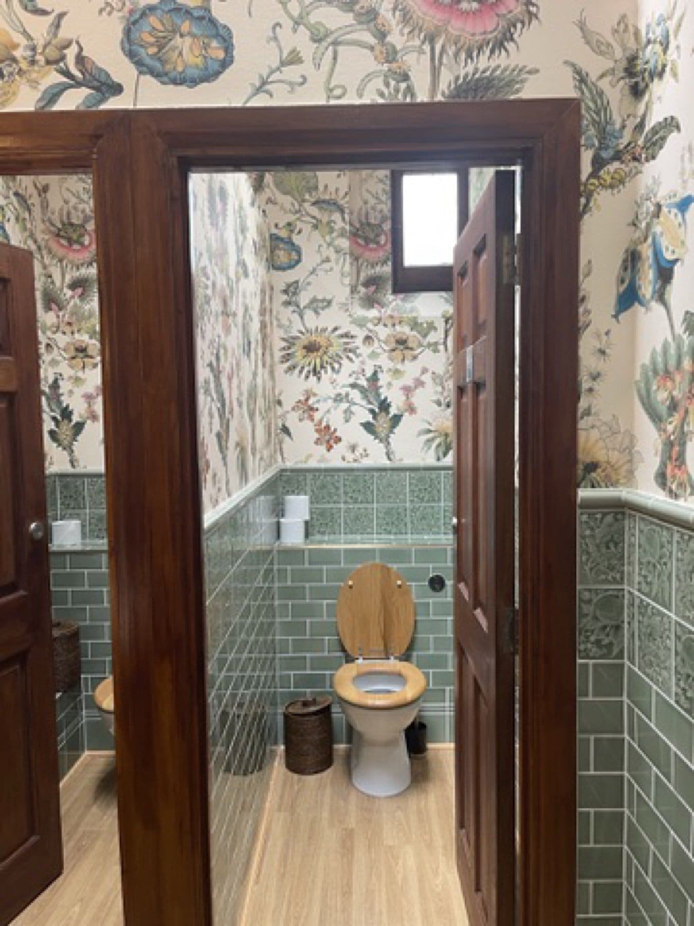 Cloakroom at the House of Hackney showroom, seen through a doorway, with floral wallpaper above green tiles.