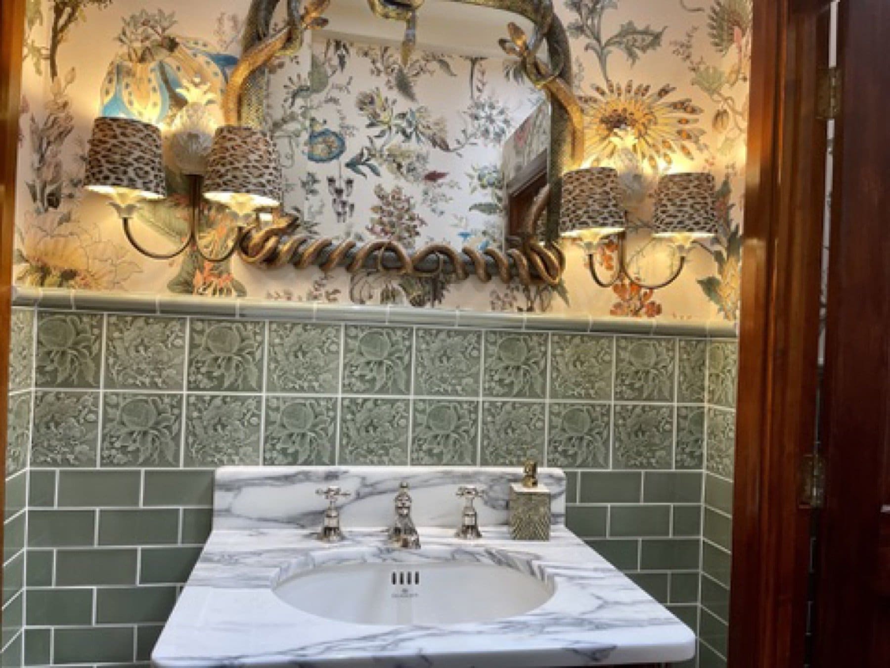 Cloakroom basin at the House of Hackney showroom, with floral wallpaper above green tiles and a marble vanity.