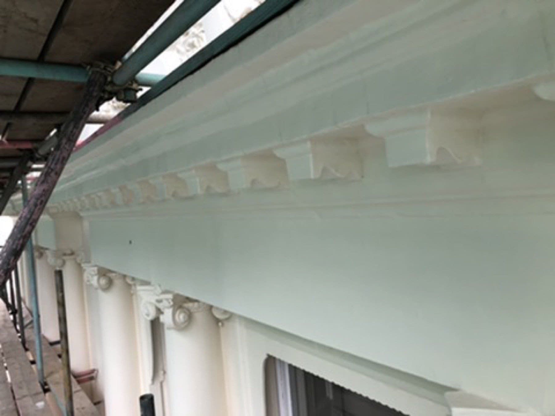 Upper facade on Inverness Terrace under scaffold, with a stucco cornice, balcony brackets and a black iron railing.