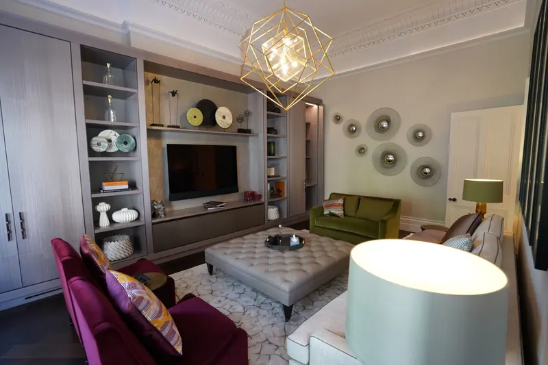 The drawing room towards its joinery wall, with a pale wallcovering behind a group of round wall mirrors and a green velvet sofa.