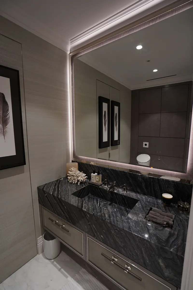 A cloakroom lined in a fine horizontal-weave wallcovering, with a black marble basin and a backlit mirror.