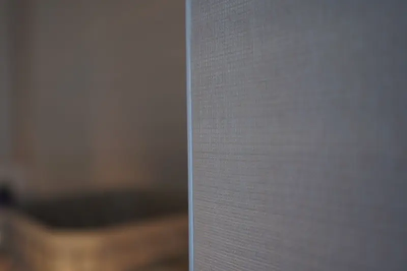 Close detail of a finished external edge: a fine woven wallcovering runs straight and tight to a crisp corner line.