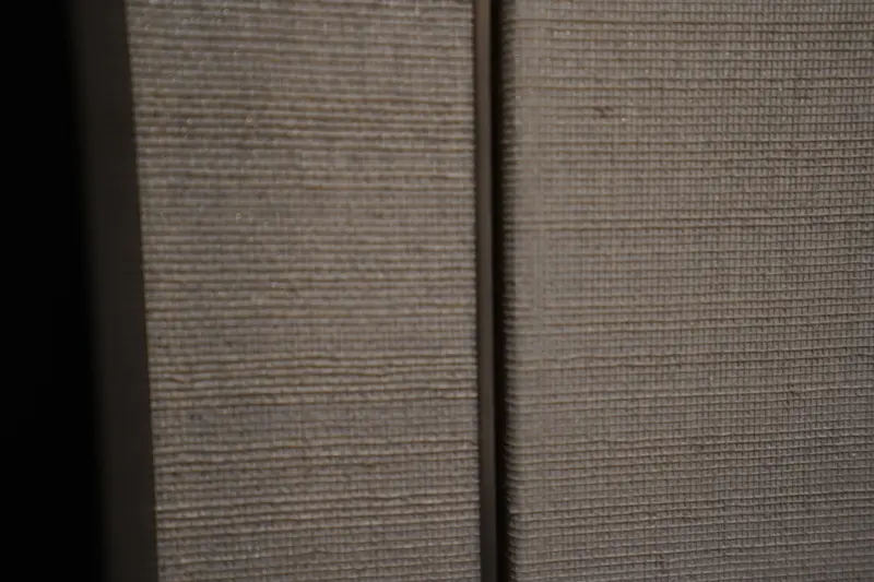Close detail of a woven wallcovering on two neighbouring surfaces, each edge cut clean either side of a narrow shadow gap.