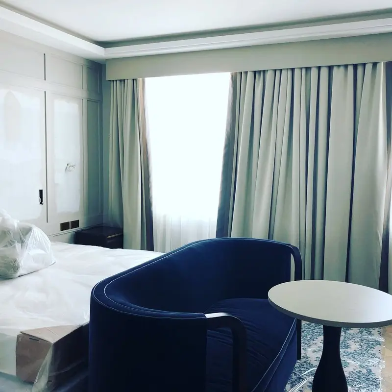 Hotel bedroom with grasscloth-effect wallcovering, navy armchair and full-height curtains, the Millennium Hotel, Grosvenor Square, now The Biltmore Mayfair.