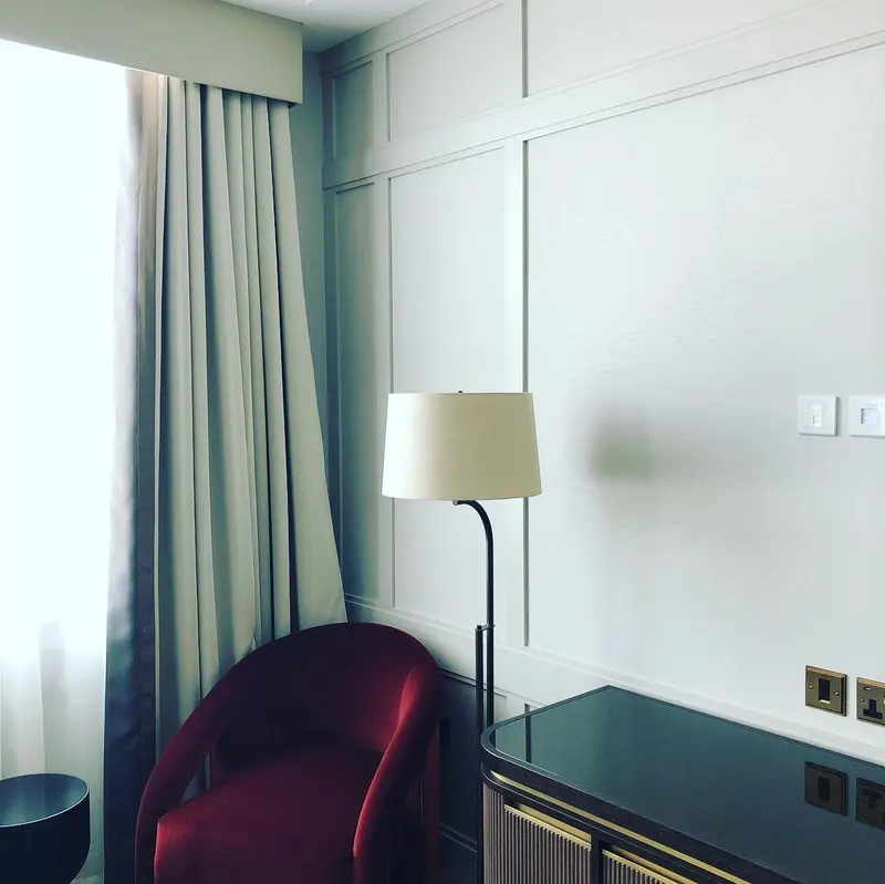 Hotel room with textured neutral wallcovering behind a desk, lamp and red armchair, the Millennium Hotel, Grosvenor Square, now The Biltmore Mayfair.