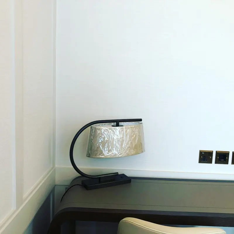 Desk corner of a hotel room with neutral textured wallcovering and a brass lamp, the Millennium Hotel, Grosvenor Square, now The Biltmore Mayfair.