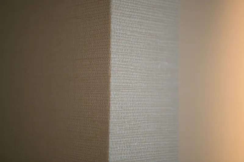 Close detail of a woven grasscloth wallcovering turning an external corner, the weave running straight and tight to the edge.