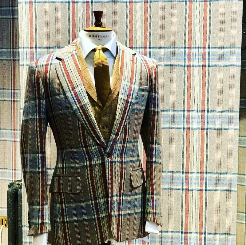 Tweed suit jacket on a stand in front of a matching Huntsman tweed-print display board.