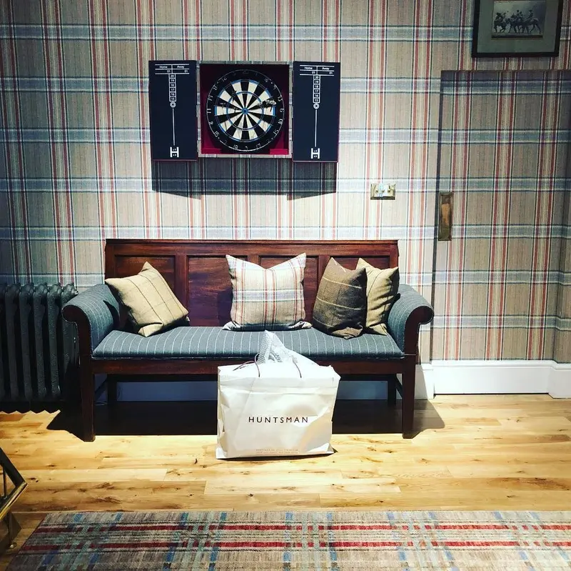 Huntsman, Savile Row: a tweed-print wallpapered room with a sofa and dartboard.