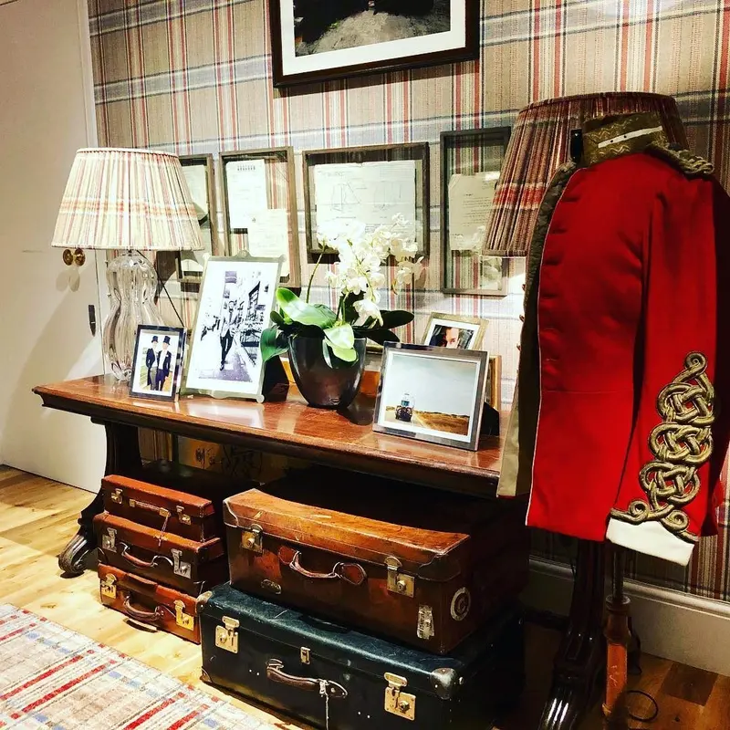 Huntsman, Savile Row: a display with a red coat and luggage against tweed-print walls.