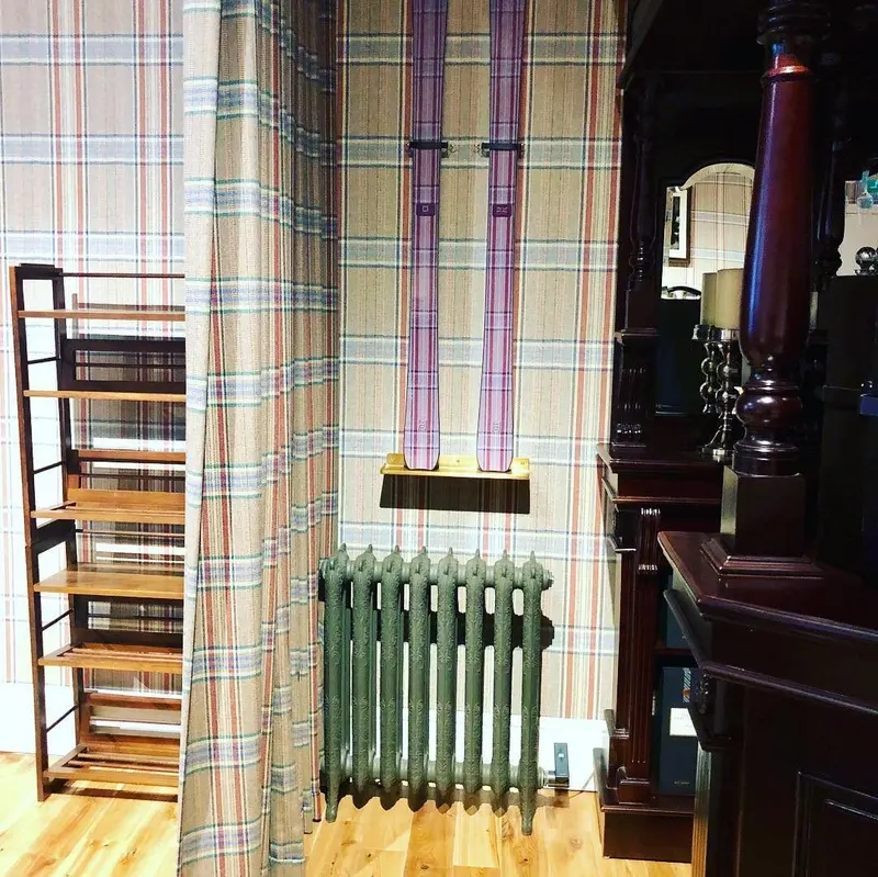Huntsman, Savile Row: tweed-print walls with a column radiator and timber shelving.