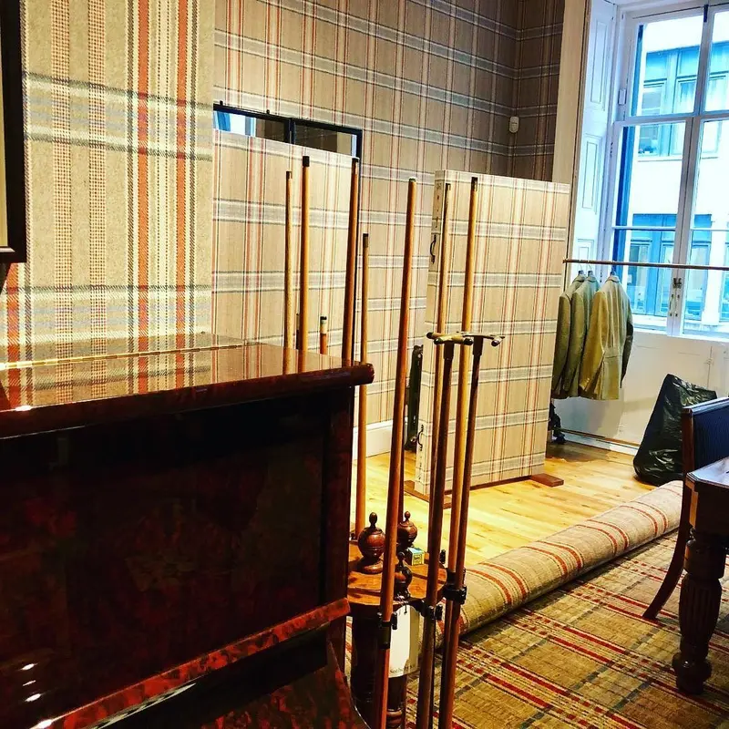 Huntsman, Savile Row: fitting room with tweed-print wallpaper and dark joinery.
