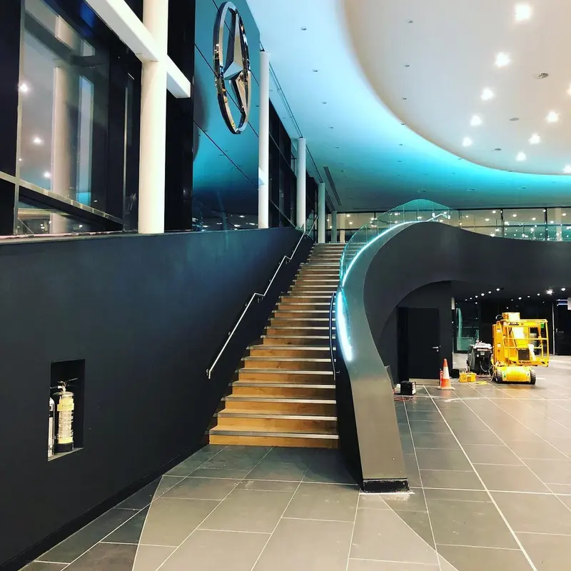 Curved staircase beside walls finished in black matt wallcovering, Mercedes-AMG showroom, London.