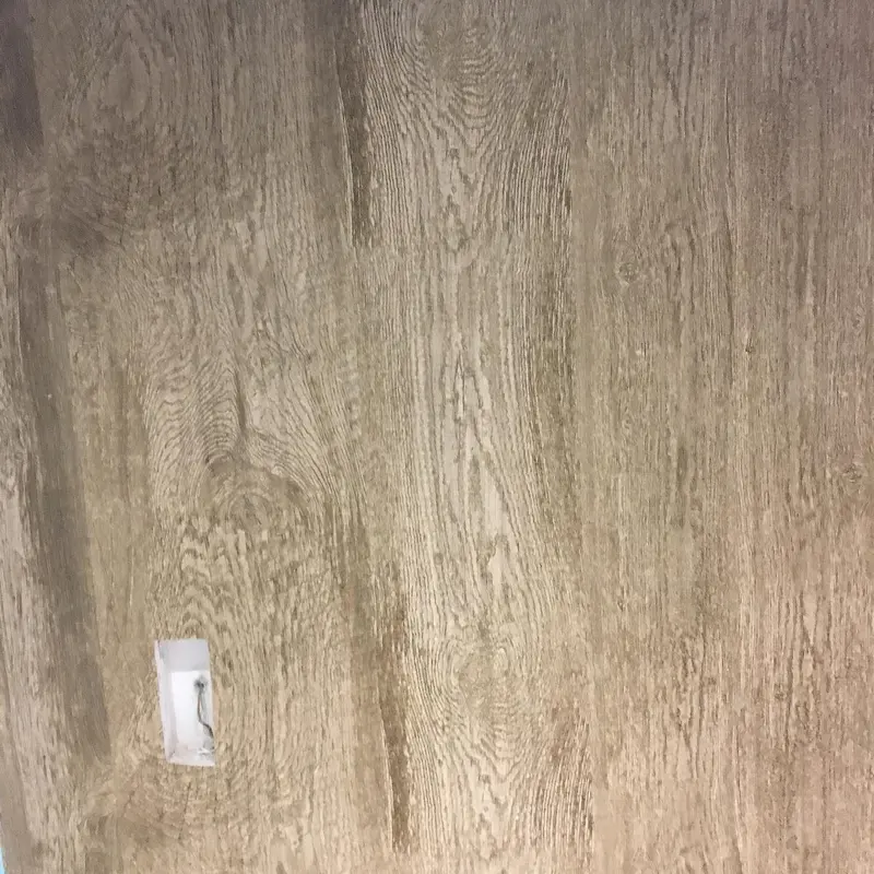 Close-up of a timber-grain wallcovering beside a light switch, Novotel London Canary Wharf.