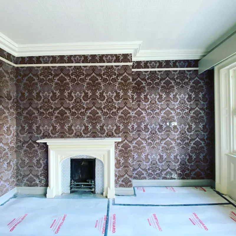 Pendley Manor bedroom papered in a dark damask with a white fireplace, floor protected.