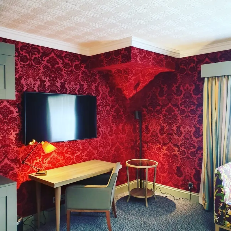 Pendley Manor bedroom with red damask walls, upholstered headboard and red bedside lamps.