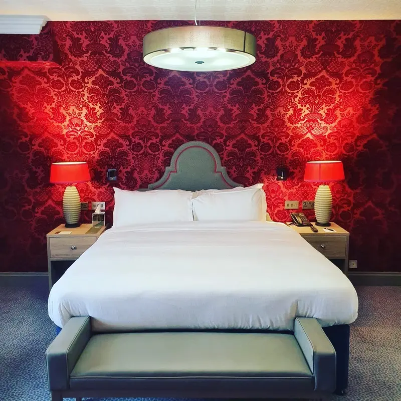 Pendley Manor guest room with red damask wallpaper, a desk and wall-mounted TV.