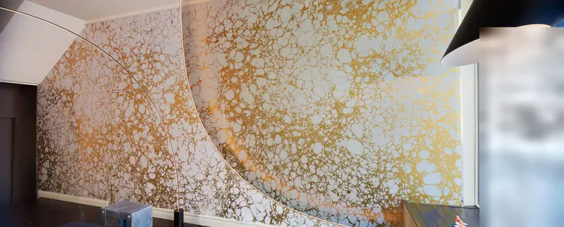 Panorama of the marbled showroom wall, the gilded pattern running unbroken across the full length of the room.