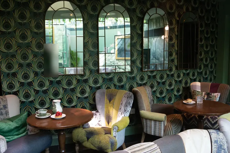 The feather wallpaper behind three arched mirrors, the large-scale pattern running unbroken around them above the tables and armchairs.