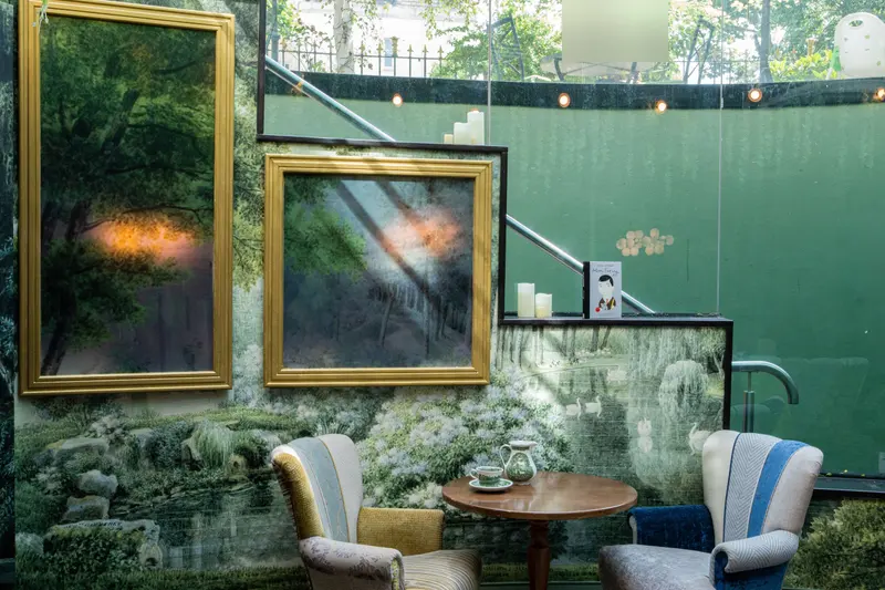 The garden room: a panoramic scenic wallpaper of a swan lake and flowering hydrangeas, with gilt-framed mirrors, two armchairs and a tea table.