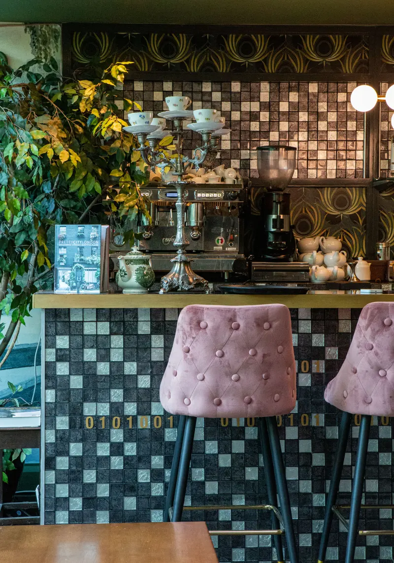 The tea counter: the feather wallpaper above a tiled bar, with an espresso machine, a silver cake stand and pink velvet stools.
