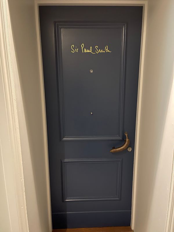 Navy-painted guest-room door at Brown's Hotel, Mayfair, lettered 'Sir Paul Smith' in gold, with a brass lever handle.