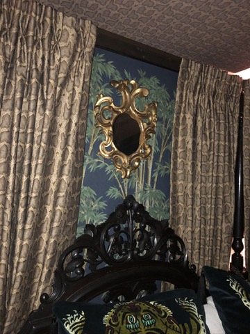 Bed wall with a gilt mirror on Bambusa Midnight wallpaper.