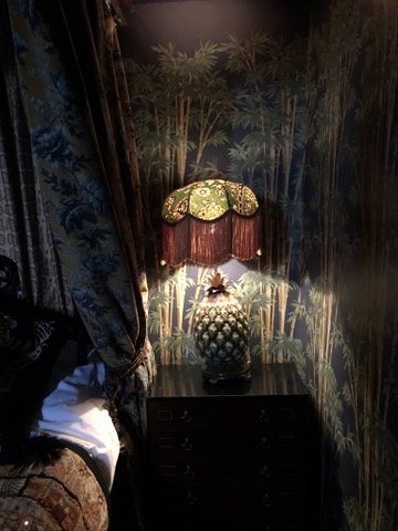 Bedside corner with a fringed lamp against Bambusa wallpaper.