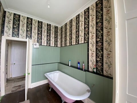 Bathroom with a roll-top bath and floral stripe wallpaper at the Castle of Trematon.